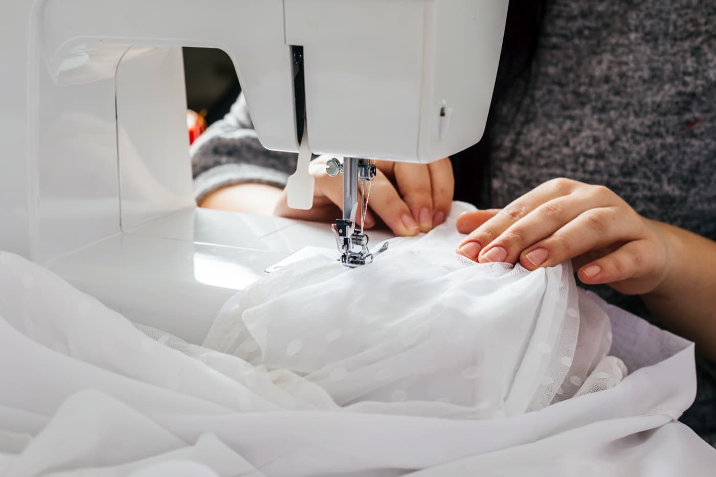 Tailor sewing a white dotted fabric on a professional sewing machine at a Los Angeles alterations studio